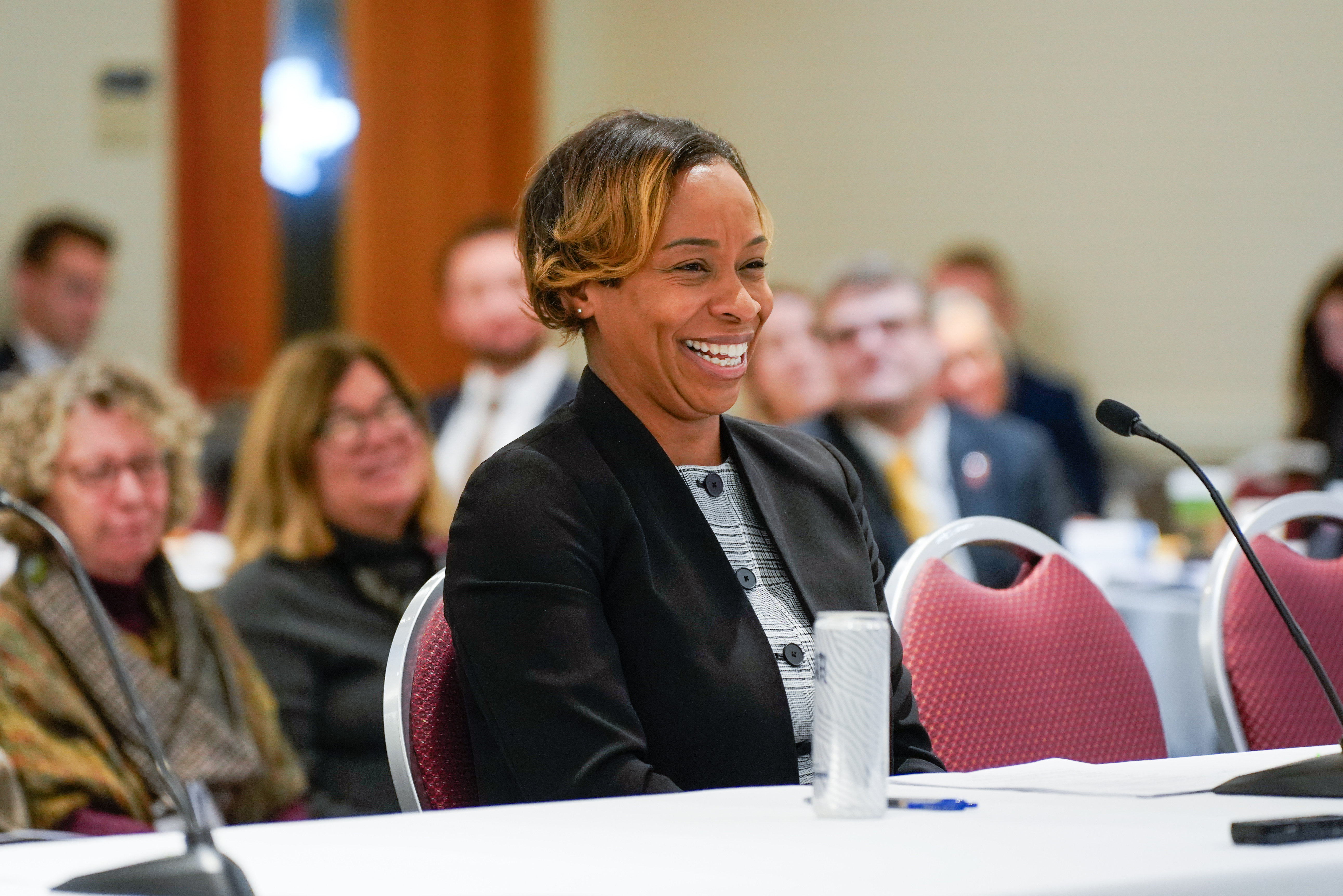 Image of Attorney General Andrea Joy Campbell at the 2025 Health Care Cost Trends Hearing during her introductory remarks. Attorney Campbell is sitting at a table and smiling in the photo. 
