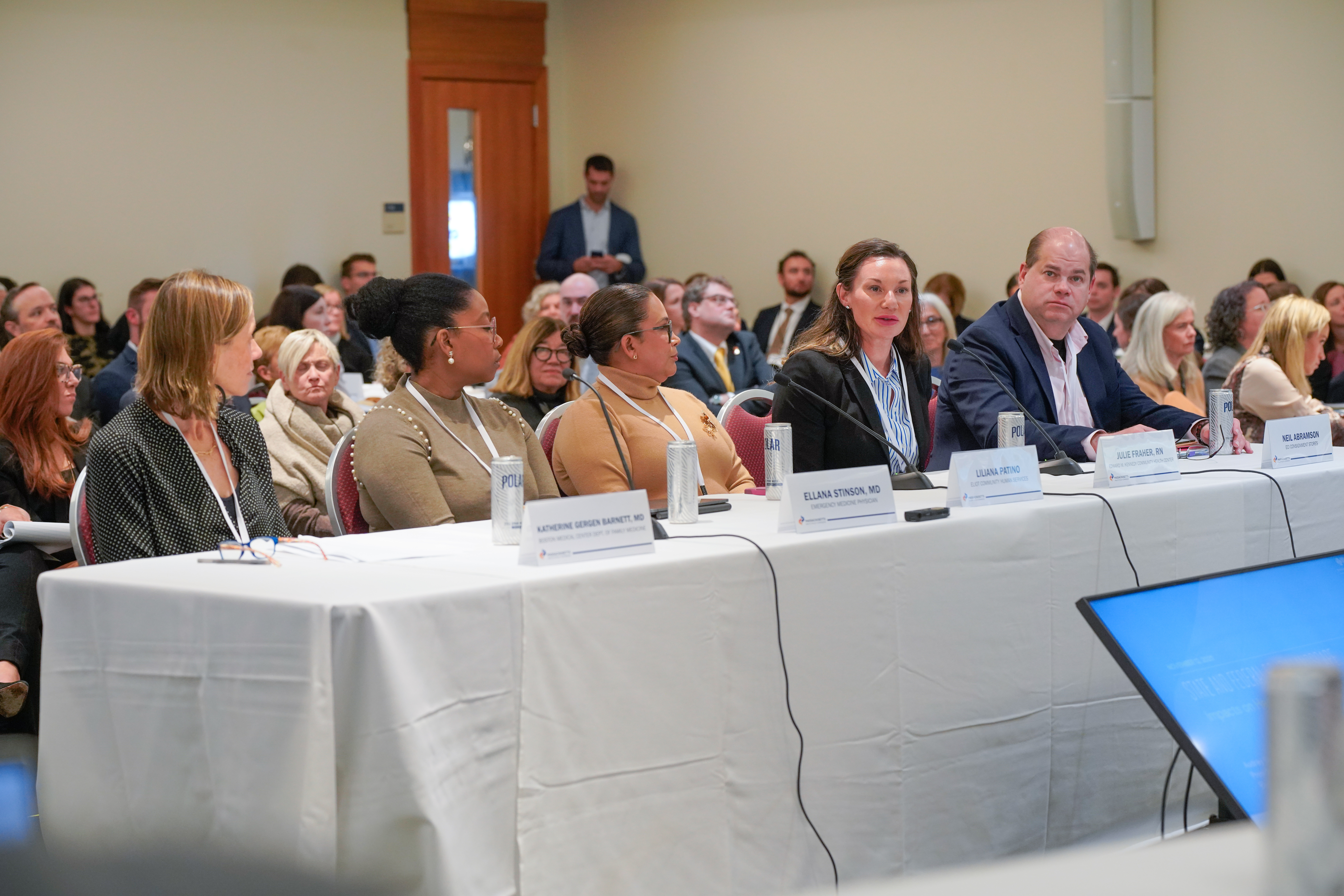 Photo of the five panelists on panel 1, sitting at a long table while providing testimony. One of the panelists is speaking into a microphone. 