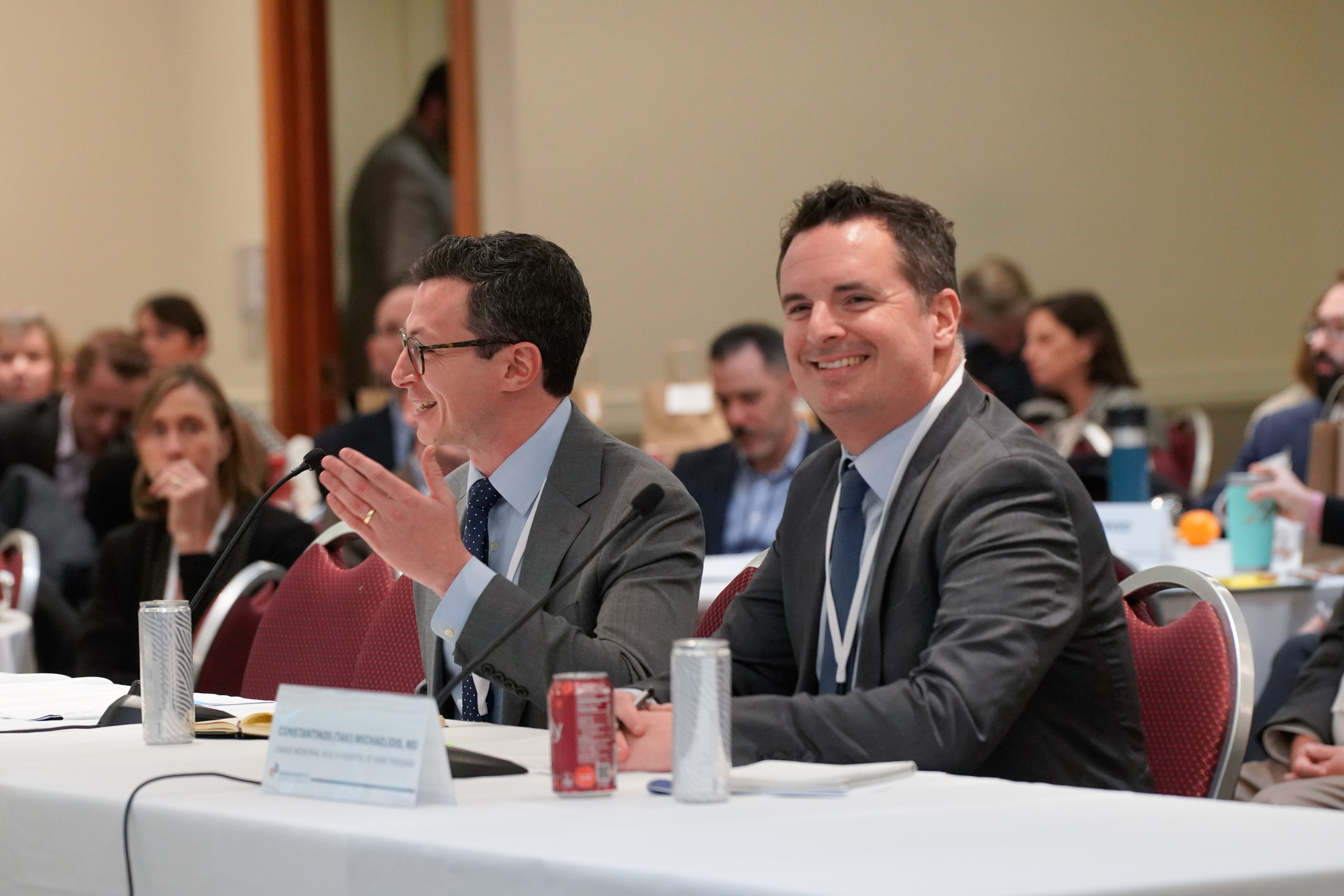 Photo of the two panelists on panel 3, one of the panelists is speaking into the microphone while the other is smiling.